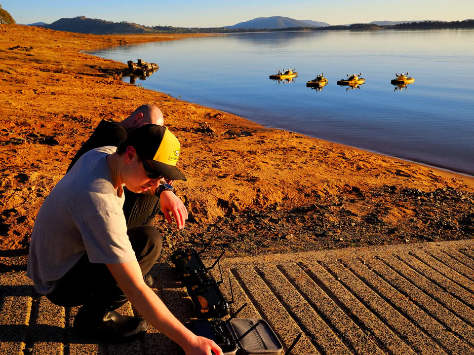 Two Surfbee operators preparing a controller beside four vehicles on the water.